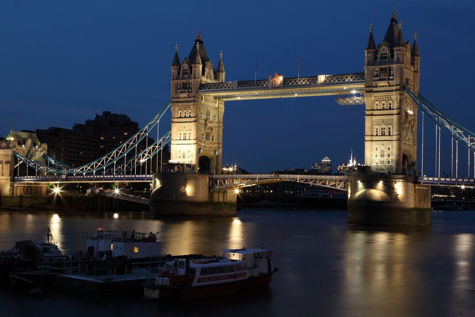 A detailed view of the Tower Bridge in London showcasing its two ornate towers constructed from stone and brick, connected by walkways and a suspension bridge with blue cables and railings. The bridge